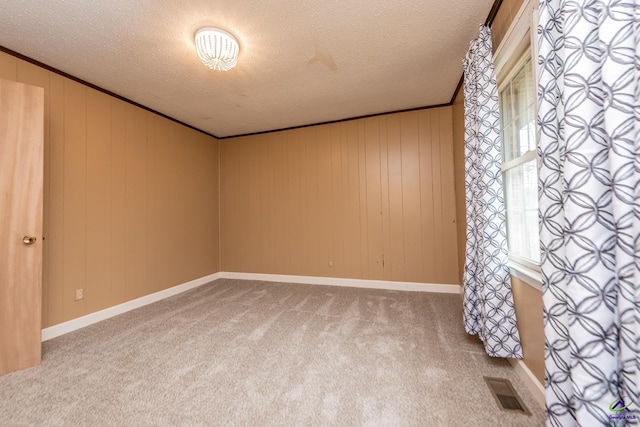 carpeted empty room featuring a textured ceiling, visible vents, and crown molding