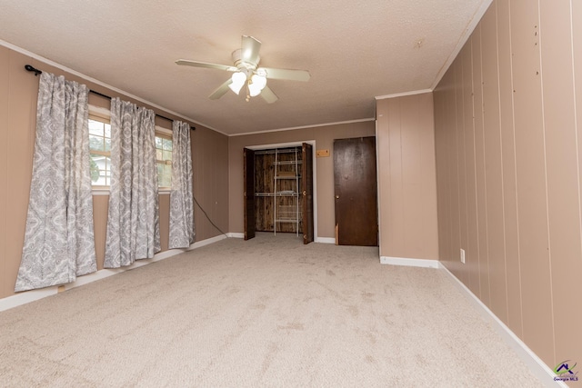 interior space featuring a textured ceiling, ceiling fan, light colored carpet, baseboards, and crown molding