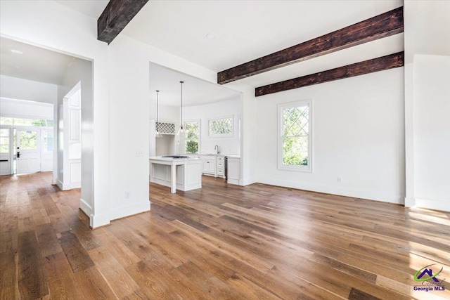 unfurnished living room with hardwood / wood-style flooring, beamed ceiling, sink, and a healthy amount of sunlight