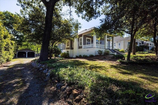 view of front facade with covered porch, a front lawn, a garage, and an outbuilding