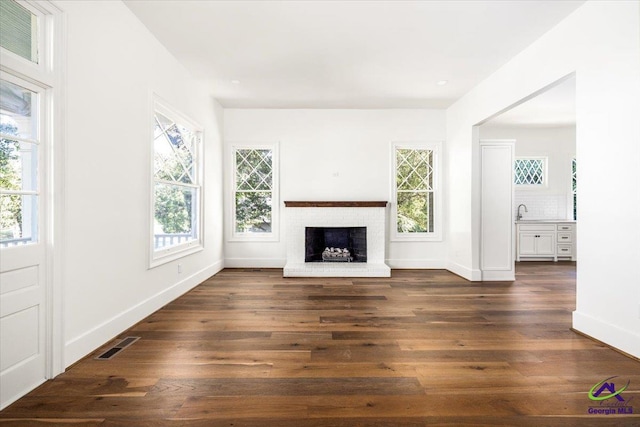 unfurnished living room with sink, a brick fireplace, dark hardwood / wood-style floors, and plenty of natural light