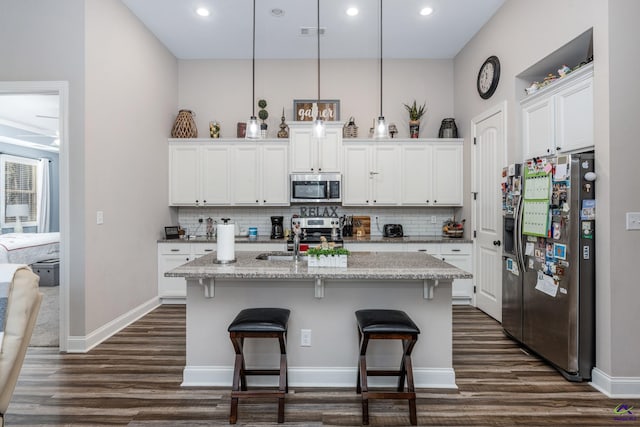 kitchen featuring a center island with sink, light stone counters, white cabinetry, decorative light fixtures, and stainless steel appliances