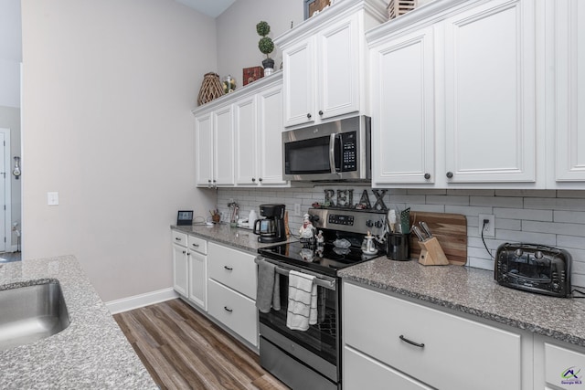 kitchen with stainless steel appliances, dark hardwood / wood-style flooring, light stone countertops, sink, and white cabinets