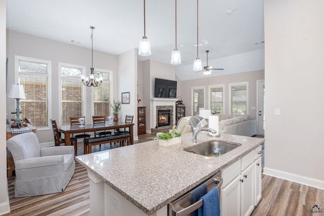 kitchen featuring an island with sink, white cabinets, stainless steel dishwasher, decorative light fixtures, and sink