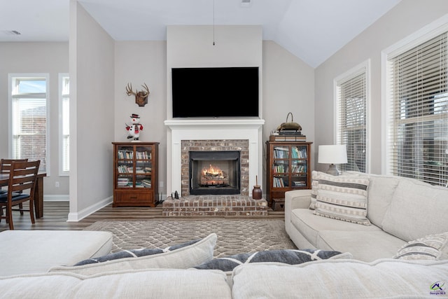 living room with a brick fireplace, vaulted ceiling, and wood-type flooring