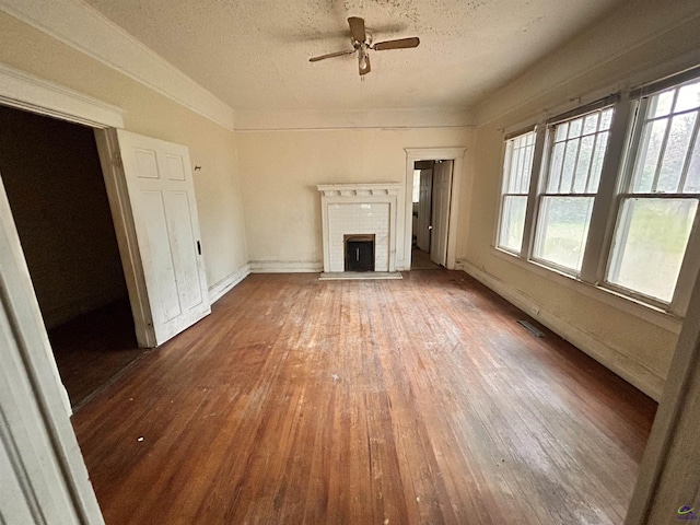 unfurnished living room featuring a textured ceiling, hardwood / wood-style flooring, a brick fireplace, and a healthy amount of sunlight