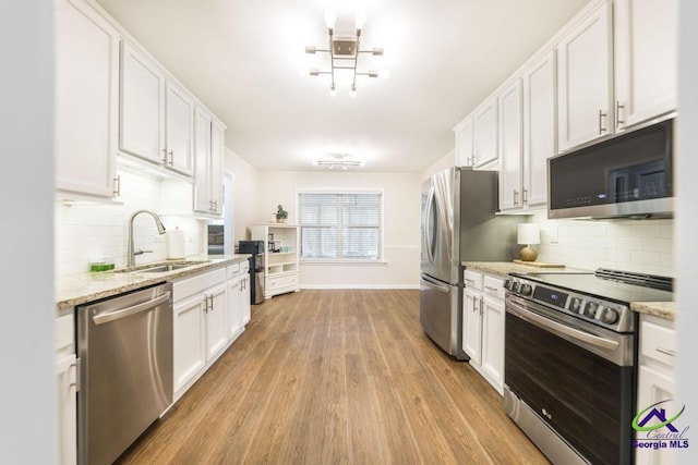 kitchen with white cabinets, appliances with stainless steel finishes, sink, and light stone counters