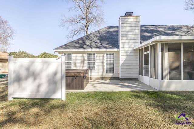 back of property with a hot tub, a patio, a sunroom, and a yard