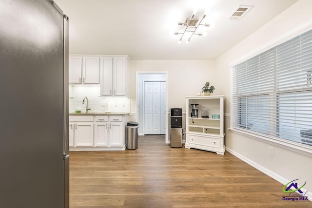 kitchen featuring sink, white cabinetry, light hardwood / wood-style floors, stainless steel fridge, and tasteful backsplash