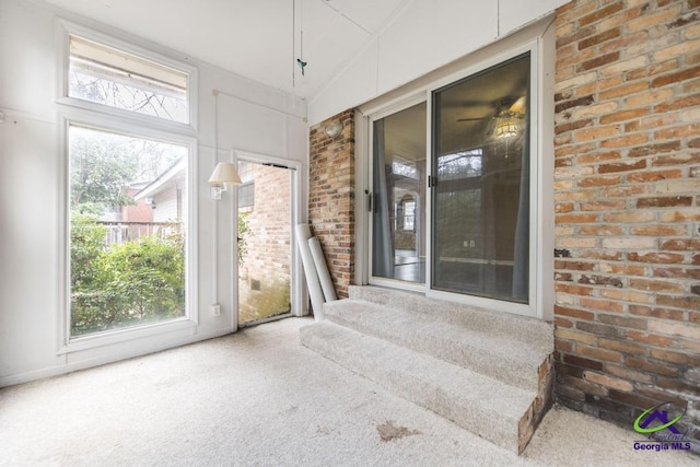 interior space with lofted ceiling, carpet flooring, and brick wall