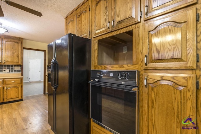 kitchen featuring light wood-type flooring, black appliances, backsplash, ceiling fan, and a textured ceiling