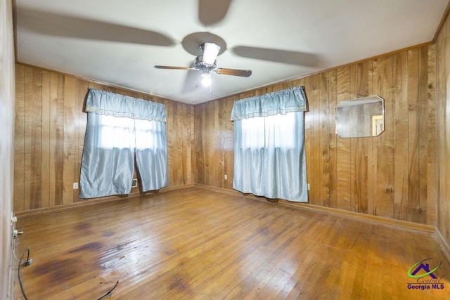 unfurnished room with hardwood / wood-style flooring, wood walls, and ceiling fan