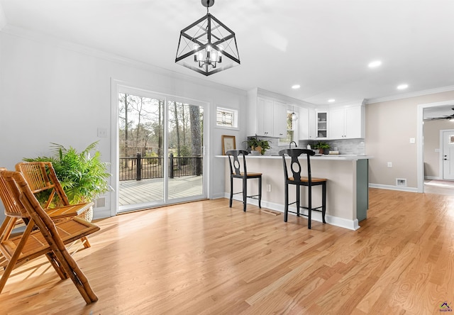 kitchen featuring pendant lighting, crown molding, light wood-type flooring, white cabinetry, and kitchen peninsula