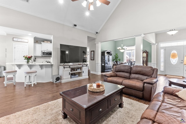 living room with high vaulted ceiling, crown molding, decorative columns, and hardwood / wood-style floors