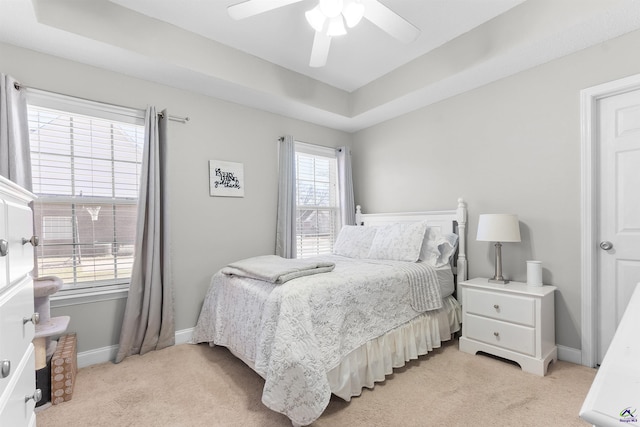 bedroom with ceiling fan, a raised ceiling, and light carpet