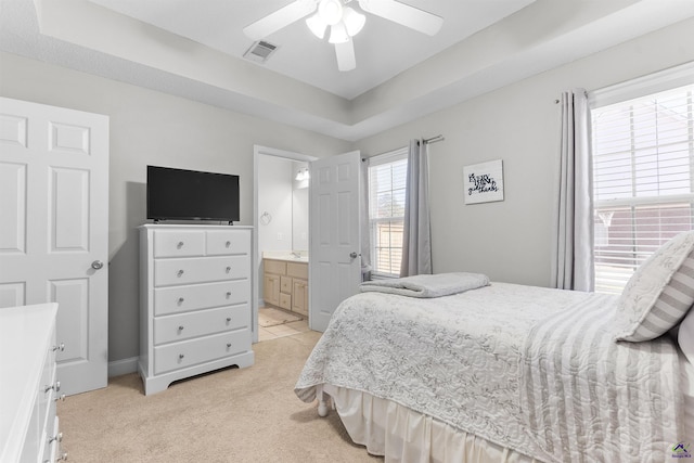 bedroom with light carpet, ensuite bath, ceiling fan, and a raised ceiling