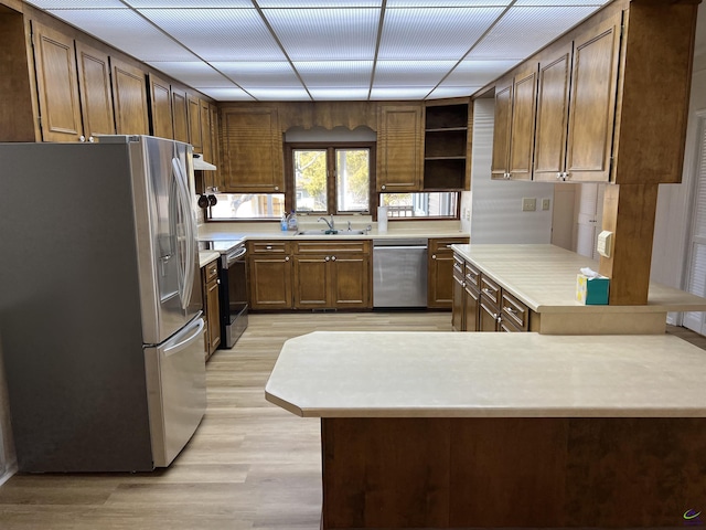 kitchen with appliances with stainless steel finishes, a peninsula, light countertops, open shelves, and a sink