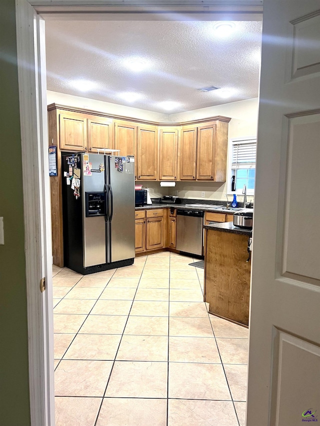 kitchen featuring light tile patterned floors, stainless steel appliances, dark countertops, and brown cabinets