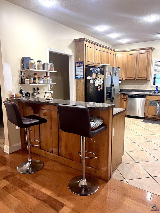 kitchen with a breakfast bar area, a peninsula, appliances with stainless steel finishes, light wood-type flooring, and dark countertops