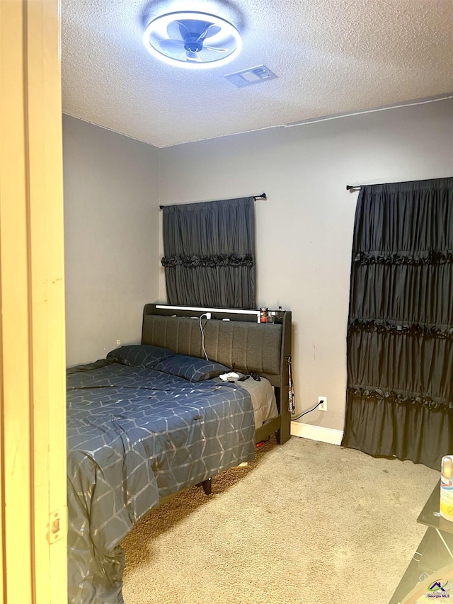 bedroom with a textured ceiling, carpet floors, visible vents, and baseboards