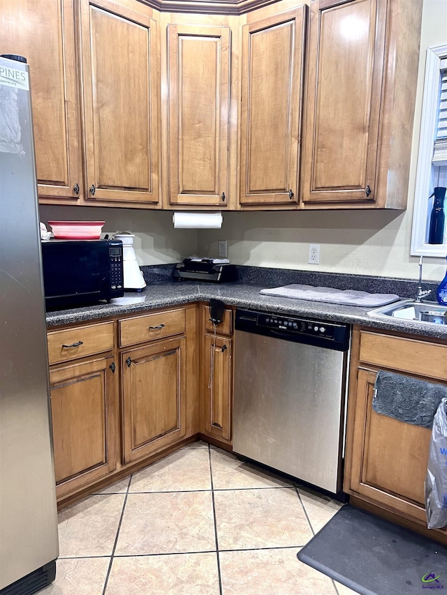 kitchen featuring light tile patterned floors, brown cabinetry, dark countertops, appliances with stainless steel finishes, and a sink