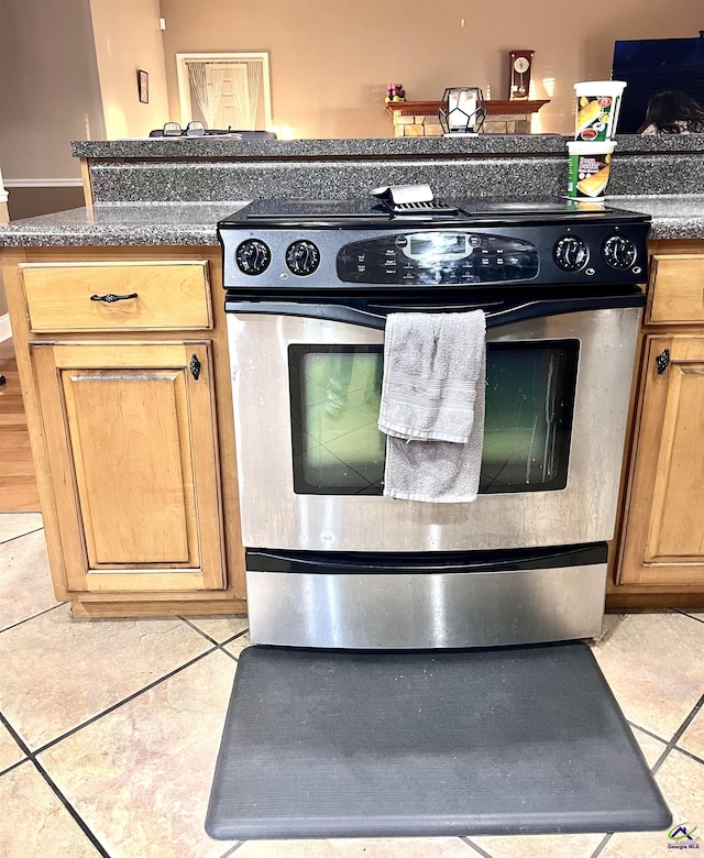 kitchen with electric stove, dark countertops, light tile patterned flooring, and brown cabinets