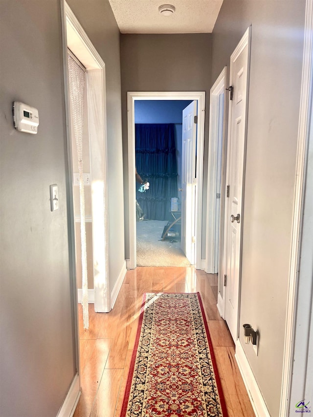 hallway with light wood-type flooring, baseboards, and a textured ceiling