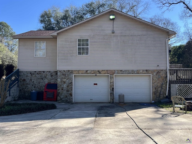 view of property exterior with a garage, concrete driveway, stone siding, stairway, and roof with shingles