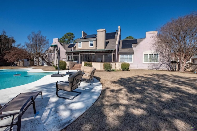 rear view of house featuring a fenced in pool, a patio, a sunroom, stairs, and roof mounted solar panels