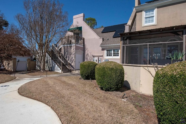 view of property exterior featuring stucco siding, a shingled roof, roof mounted solar panels, a sunroom, and stairs