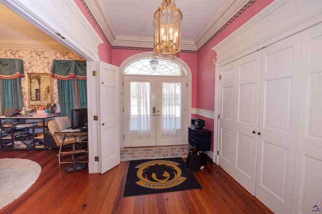 foyer entrance with wallpapered walls, ornamental molding, wood finished floors, french doors, and a notable chandelier