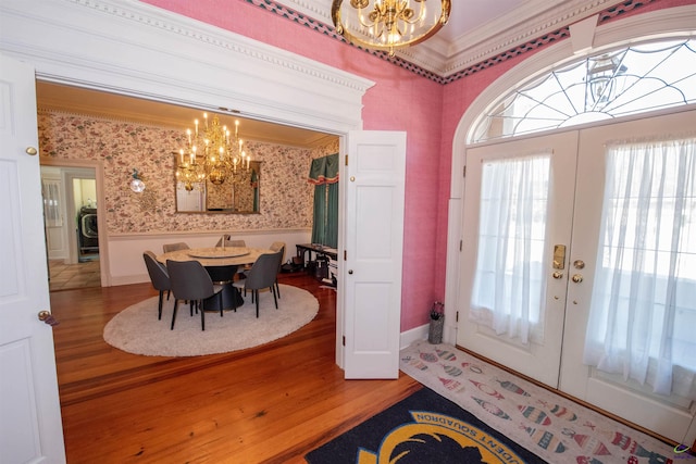 foyer entrance with a chandelier, french doors, ornamental molding, and wallpapered walls