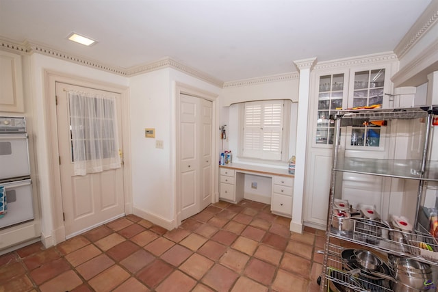 kitchen featuring ornamental molding, built in desk, white double oven, and glass insert cabinets