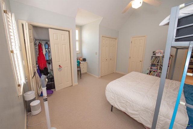 bedroom featuring light carpet, a ceiling fan, multiple closets, and lofted ceiling