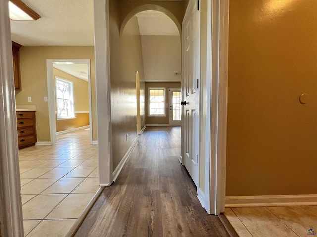 corridor featuring arched walkways, light tile patterned floors, and baseboards