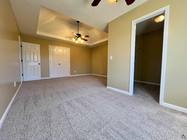 interior space with a textured ceiling, ceiling fan, a tray ceiling, and baseboards