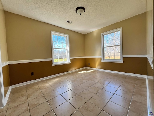 spare room featuring a textured ceiling, light tile patterned flooring, visible vents, and baseboards