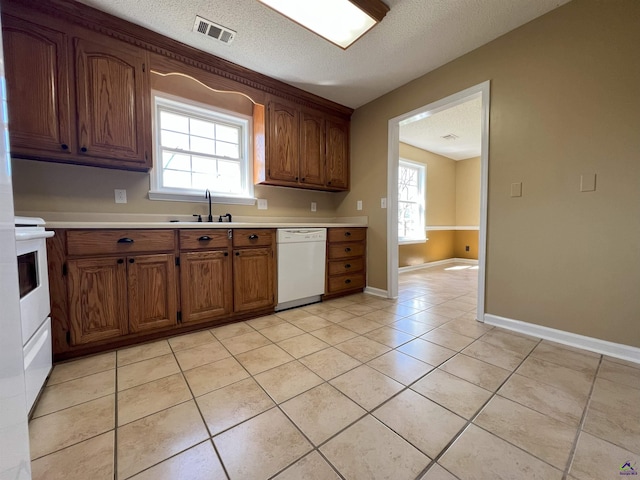 kitchen featuring light tile patterned flooring, white appliances, a sink, visible vents, and light countertops