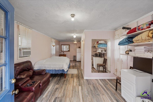 bedroom with freestanding refrigerator, cooling unit, a textured ceiling, and wood finished floors