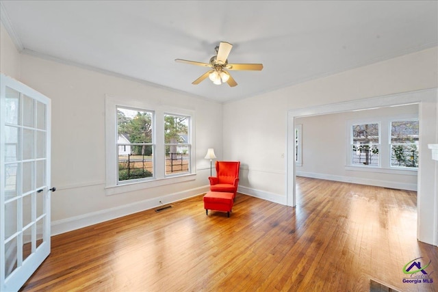 unfurnished room featuring wood finished floors, a ceiling fan, visible vents, baseboards, and ornamental molding