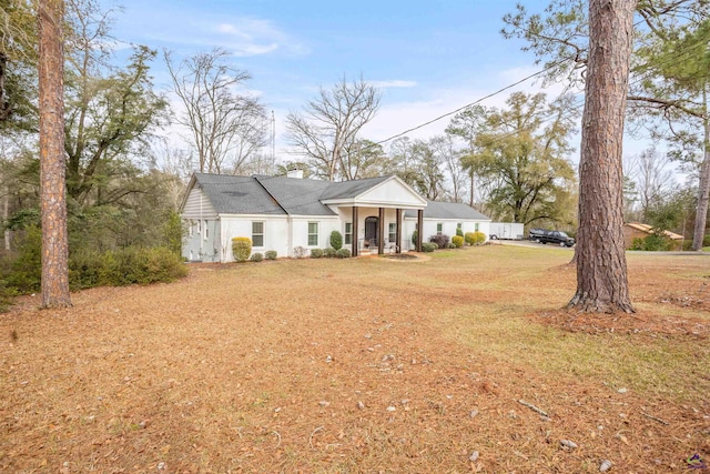 view of front of home featuring covered porch, a chimney, and a front yard