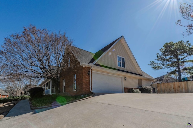 view of side of property with driveway, brick siding, an attached garage, and fence