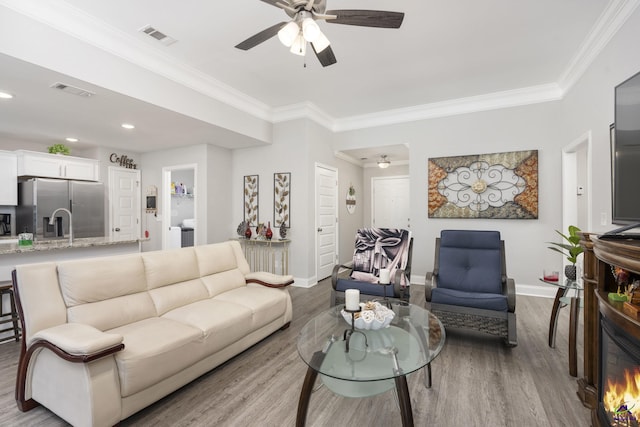 living area featuring ornamental molding, visible vents, light wood-style floors, and baseboards