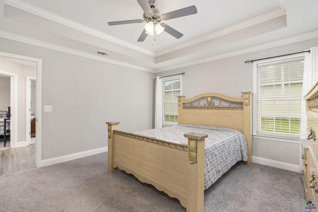 carpeted bedroom featuring baseboards, visible vents, a ceiling fan, ornamental molding, and a tray ceiling