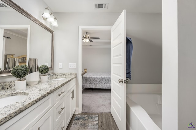 ensuite bathroom featuring double vanity, visible vents, connected bathroom, wood finished floors, and a sink