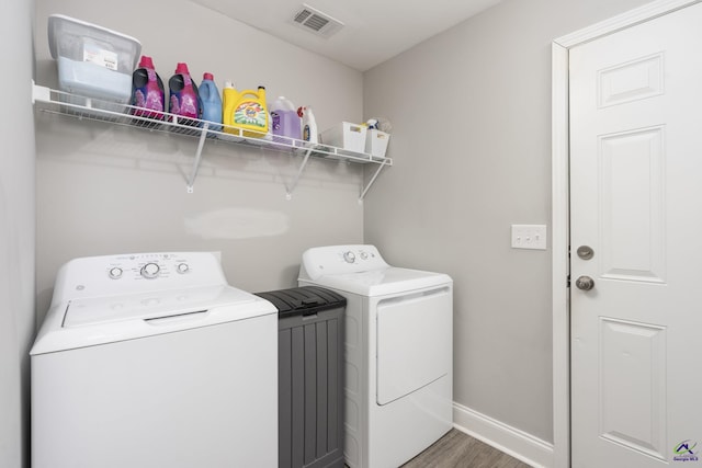 clothes washing area featuring visible vents, separate washer and dryer, wood finished floors, laundry area, and baseboards