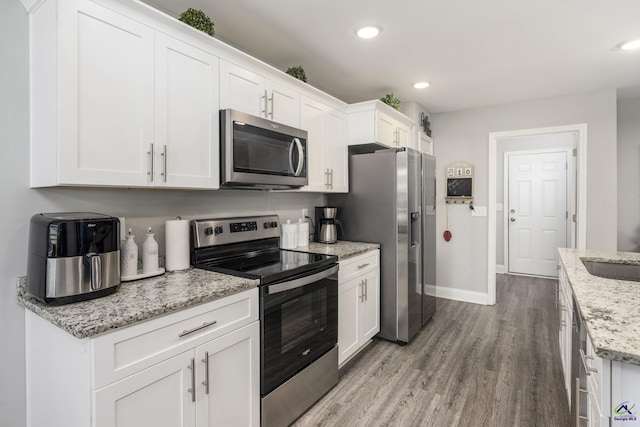 kitchen with stainless steel appliances, light stone counters, and white cabinets