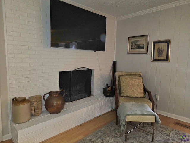 living area with a textured ceiling, wood finished floors, visible vents, ornamental molding, and a brick fireplace