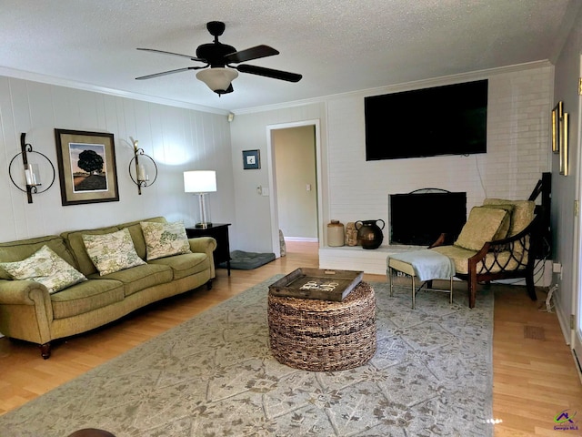 living area featuring a textured ceiling, light wood-type flooring, a ceiling fan, and crown molding