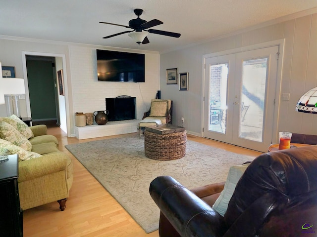 living area featuring ceiling fan, a fireplace, wood finished floors, ornamental molding, and french doors